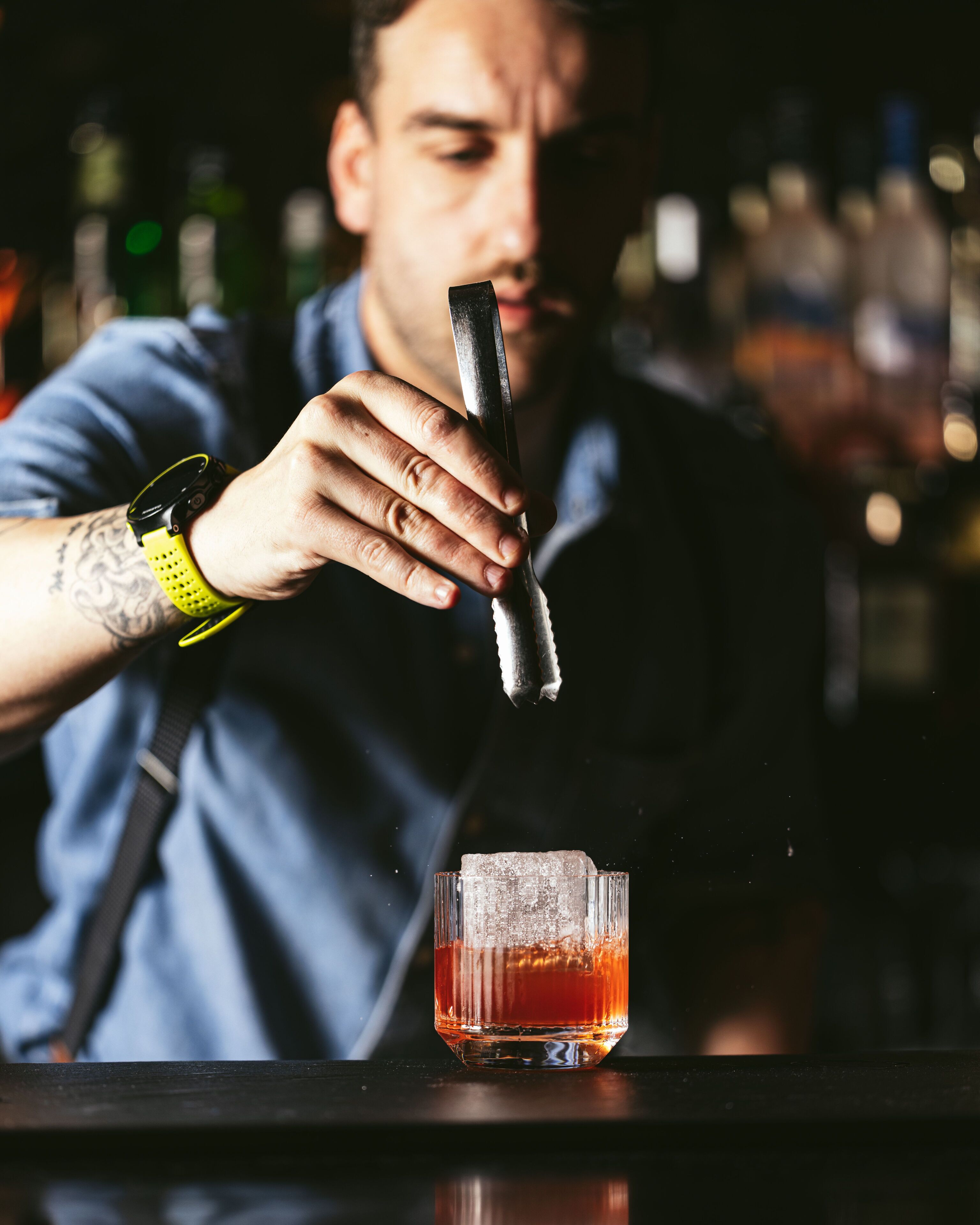 Un barman prépare un cocktail à l’aide d’un shaker et d’un verre, sur le comptoir du bar.