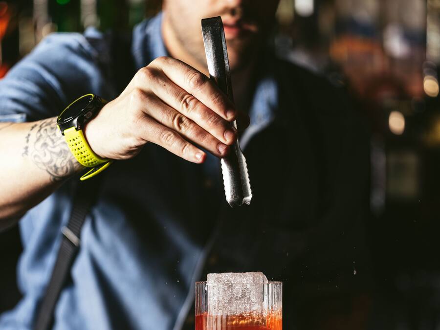 Um bartender preparando uma bebida com um coqueteleira e um copo no balcão do bar.