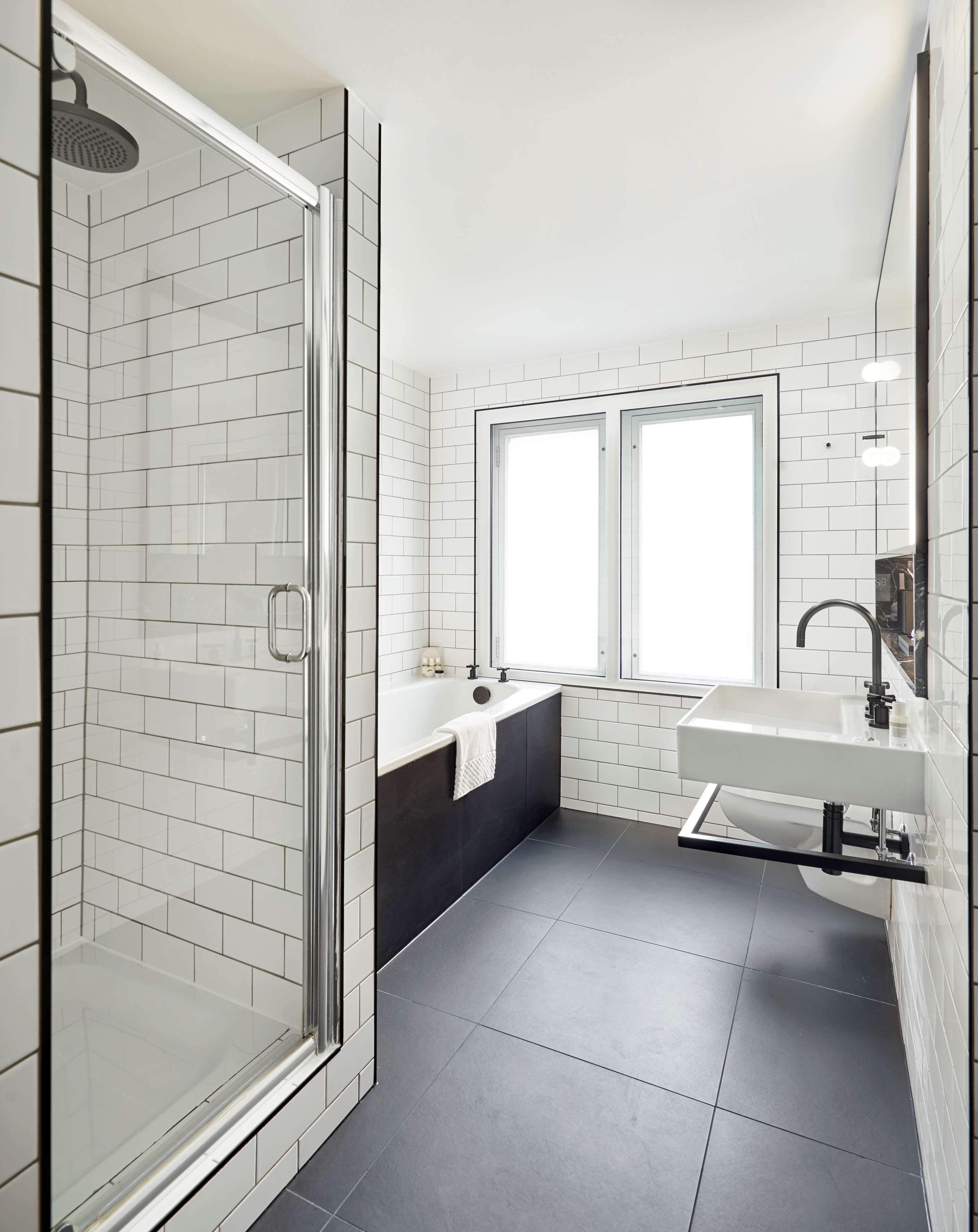 Une salle de bain moderne avec une douche à l’italienne en verre, une baignoire noire et un lavabo blanc.
