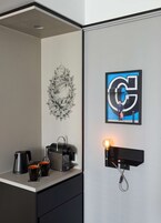 Ein modernes Zimmer mit einer Kaffeemaschine, zwei Tassen, einem Wanddekor und einem gerahmten Kunstwerk mit einem großen 'G' an der Wand.