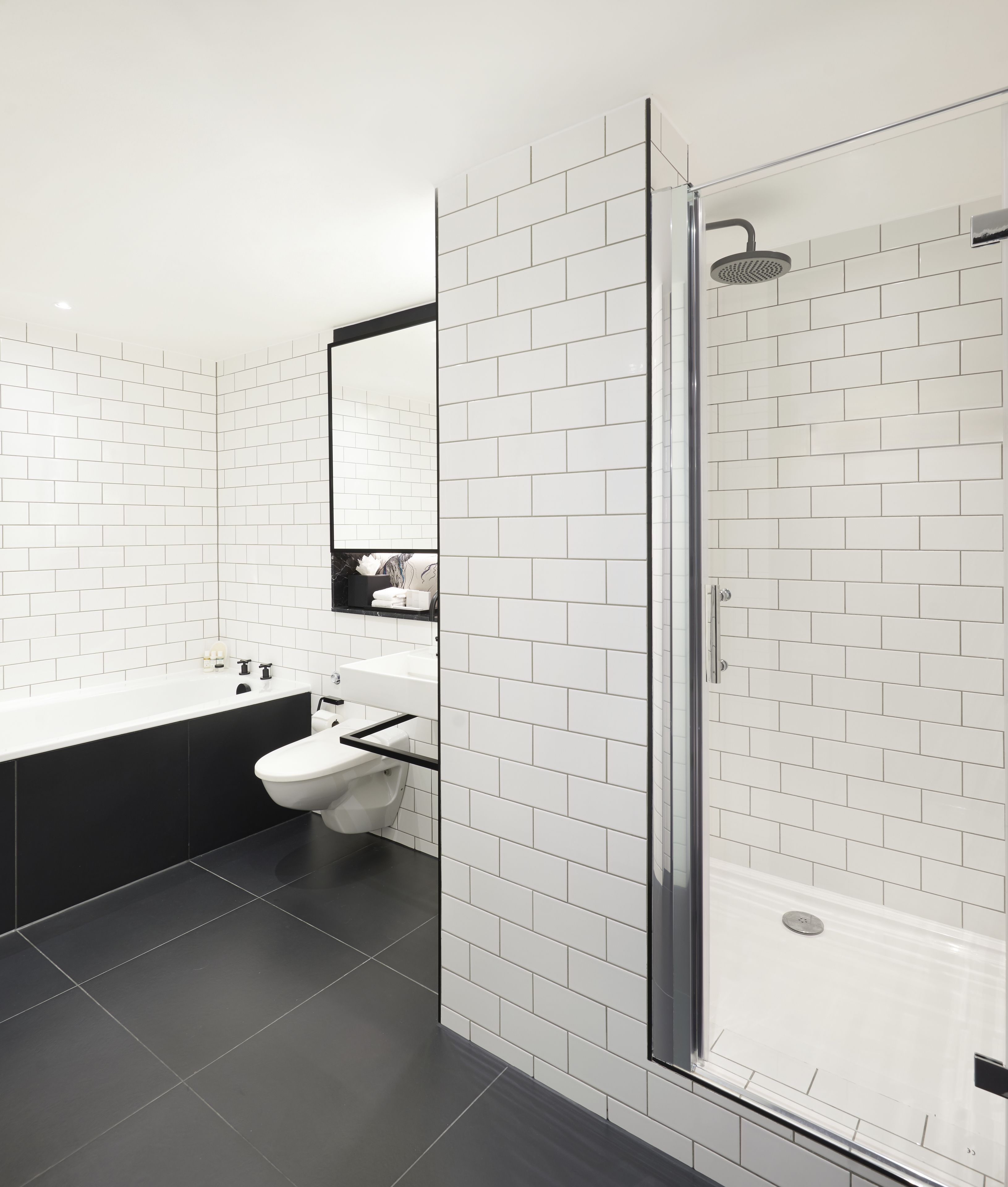 A modern bathroom with white subway tiles, a black bathtub, and a glass-enclosed shower.