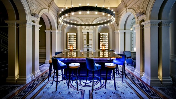 A grand dining area with a long table surrounded by blue chairs, ornate columns, and a chandelier. - ANDAZ LONDON LIVERPOOL STREET, BY HYATT (London)