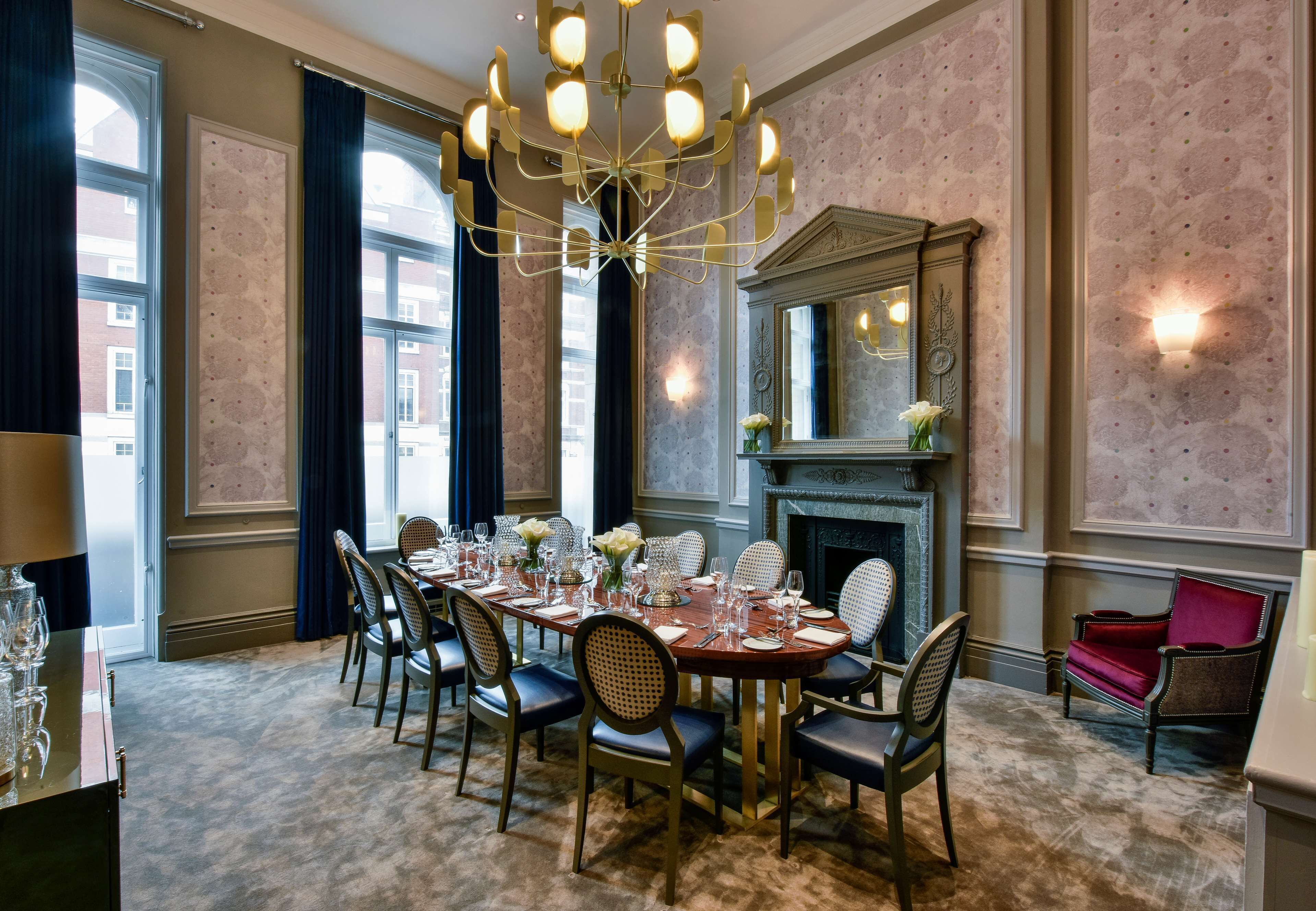 A dining room with a large table set for six, surrounded by chairs, a chandelier, and a fireplace.
