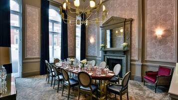 A dining room with a large table set for six, surrounded by chairs, a chandelier, and a fireplace.