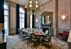Ein Esszimmer mit einem großen Tisch, gedeckt für sechs Personen, umgeben von Stühlen, einer Chandelierleuchtre und einem Kamin.