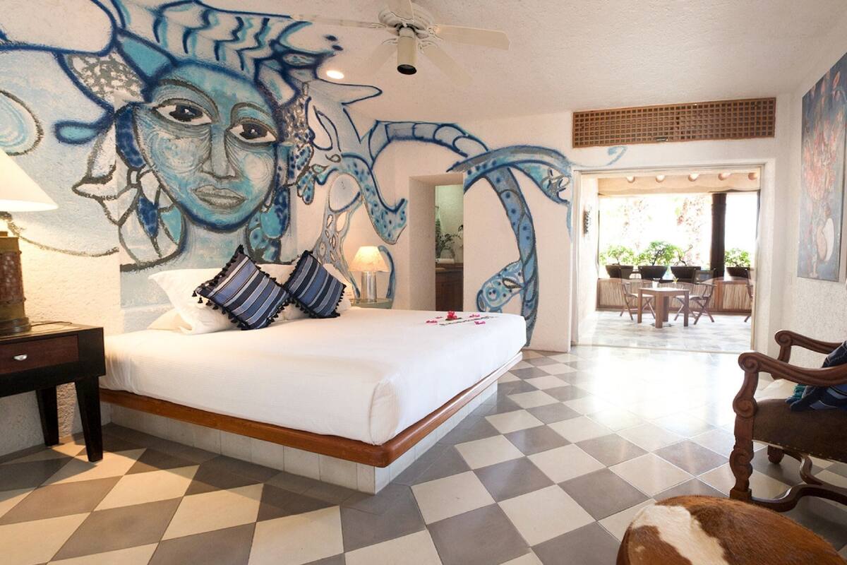 Hotelkamer met een zwart-wit geruite vloer, een bed met witte lakens, een lamp, een schilderij aan de muur en uitzicht op het buitengebied.