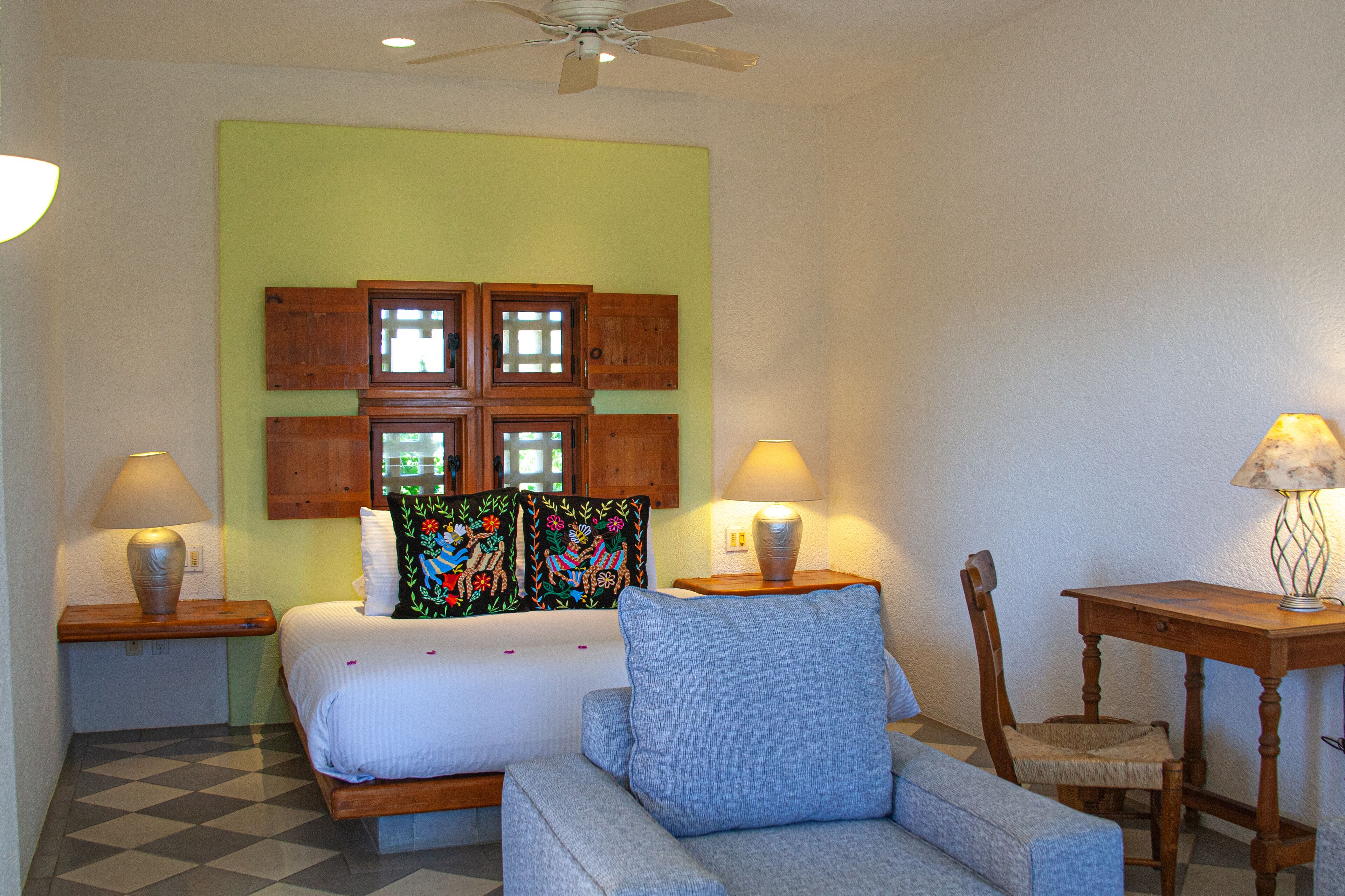 A room with a bed, two nightstands, a chair, a table, and a ceiling fan.