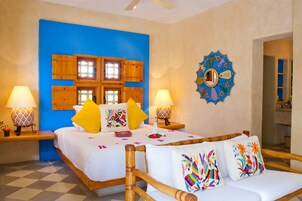 Habitación de hotel con una cama grande, cabecera de madera, dos mesitas de noche con lámparas, una pared de acento azul y un espejo decorativo.