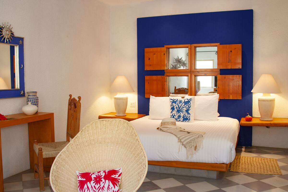 Een slaapkamer met een bed, twee nachtkastjes, een stoel, een spiegel en een blauwe accentmuur.