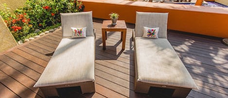 A wooden deck with two lounge chairs and a small table with a potted plant.