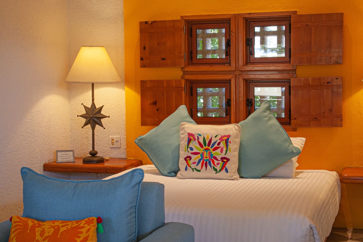 Una habitación con cama, mesita de noche, lámpara y ventana con contraventanas.