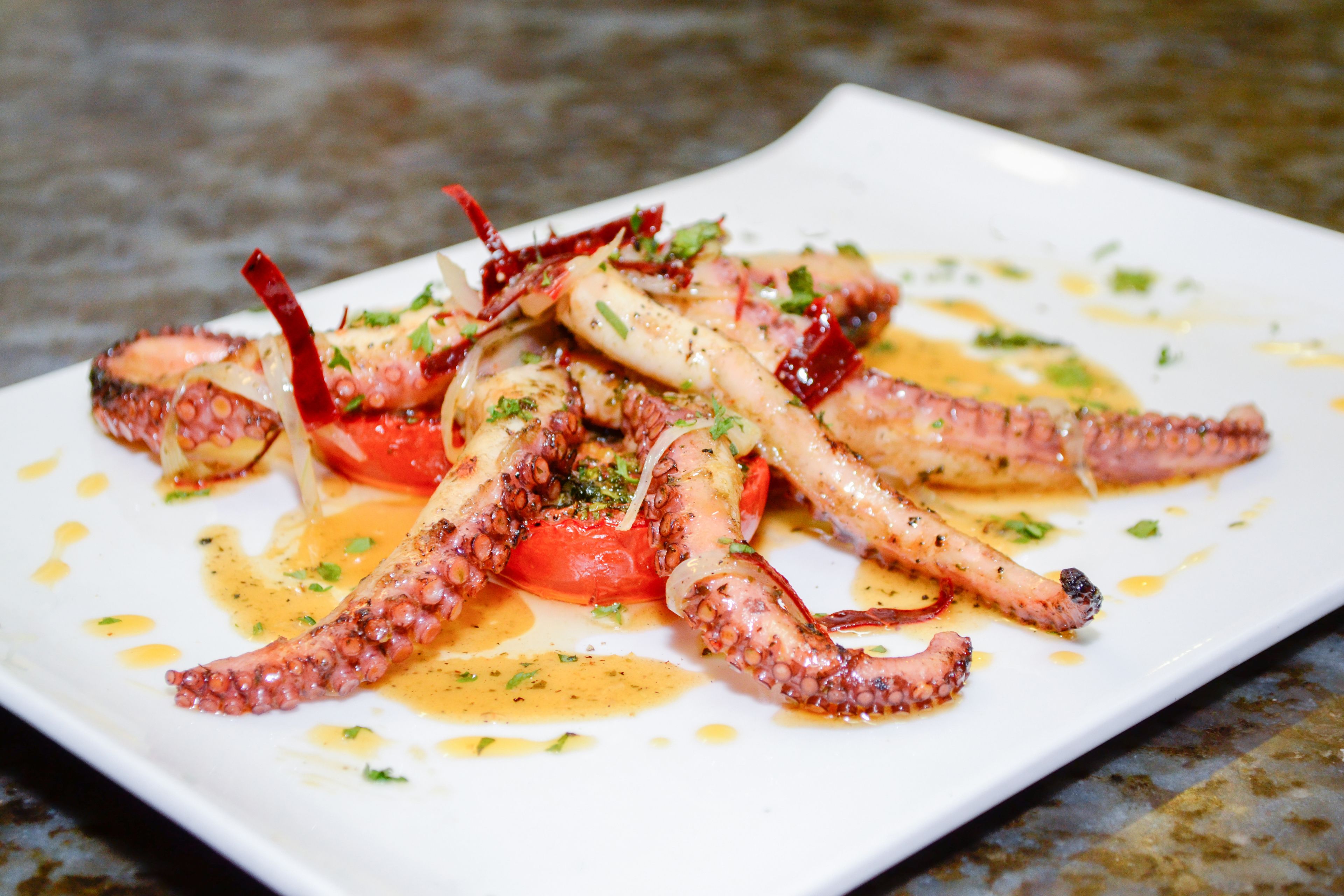 A dish of grilled octopus with tomatoes and herbs on a white plate.