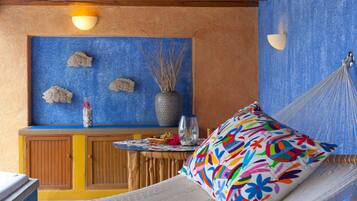 Una habitación con una hamaca, un cojín colorido, una pared azul con peces decorativos y un mueble de madera con un florero.