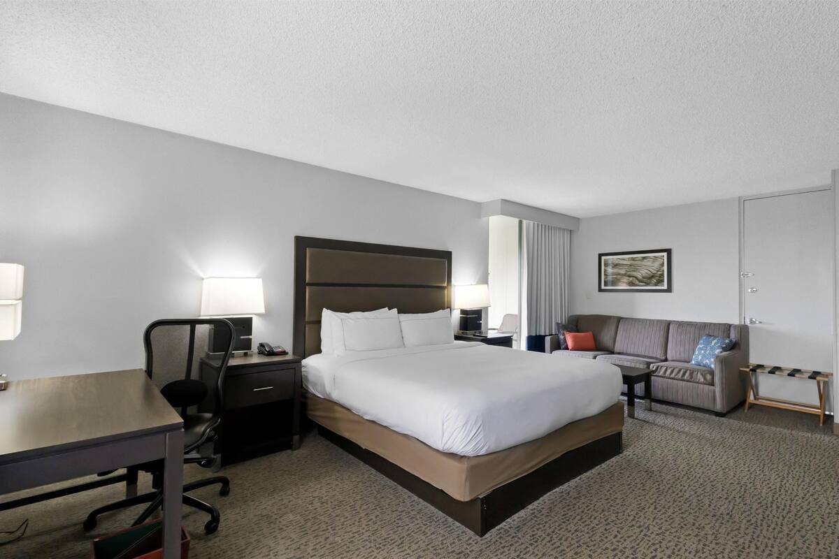 Une chambre d’hôtel avec un grand lit, un bureau avec une chaise, un canapé et une petite table.
