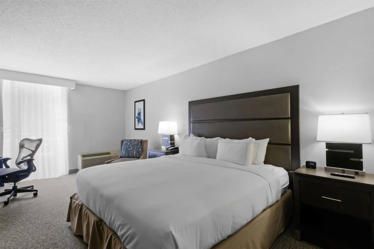 Une chambre d’hôtel avec un grand lit, un bureau avec une chaise, une table de chevet avec une lampe et un tableau au mur.
