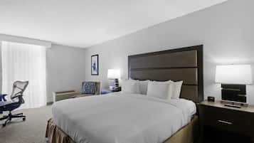Habitación de hotel con una cama grande, un escritorio con silla, una mesita de noche con lámpara y un cuadro en la pared.