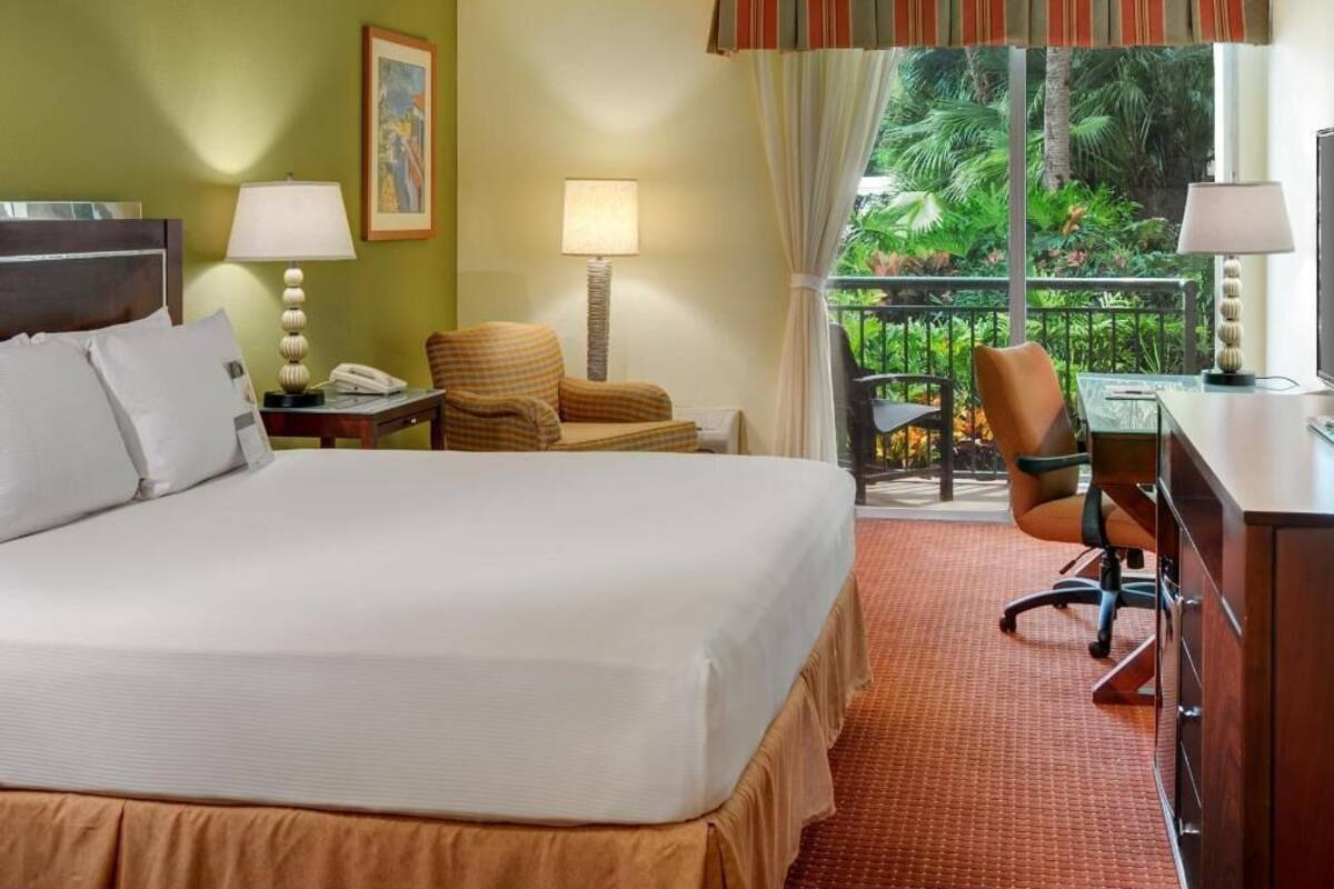 Une chambre d’hôtel équipée d’un lit, d’un bureau, d’une chaise et d’un balcon donnant sur un paysage verdoyant.