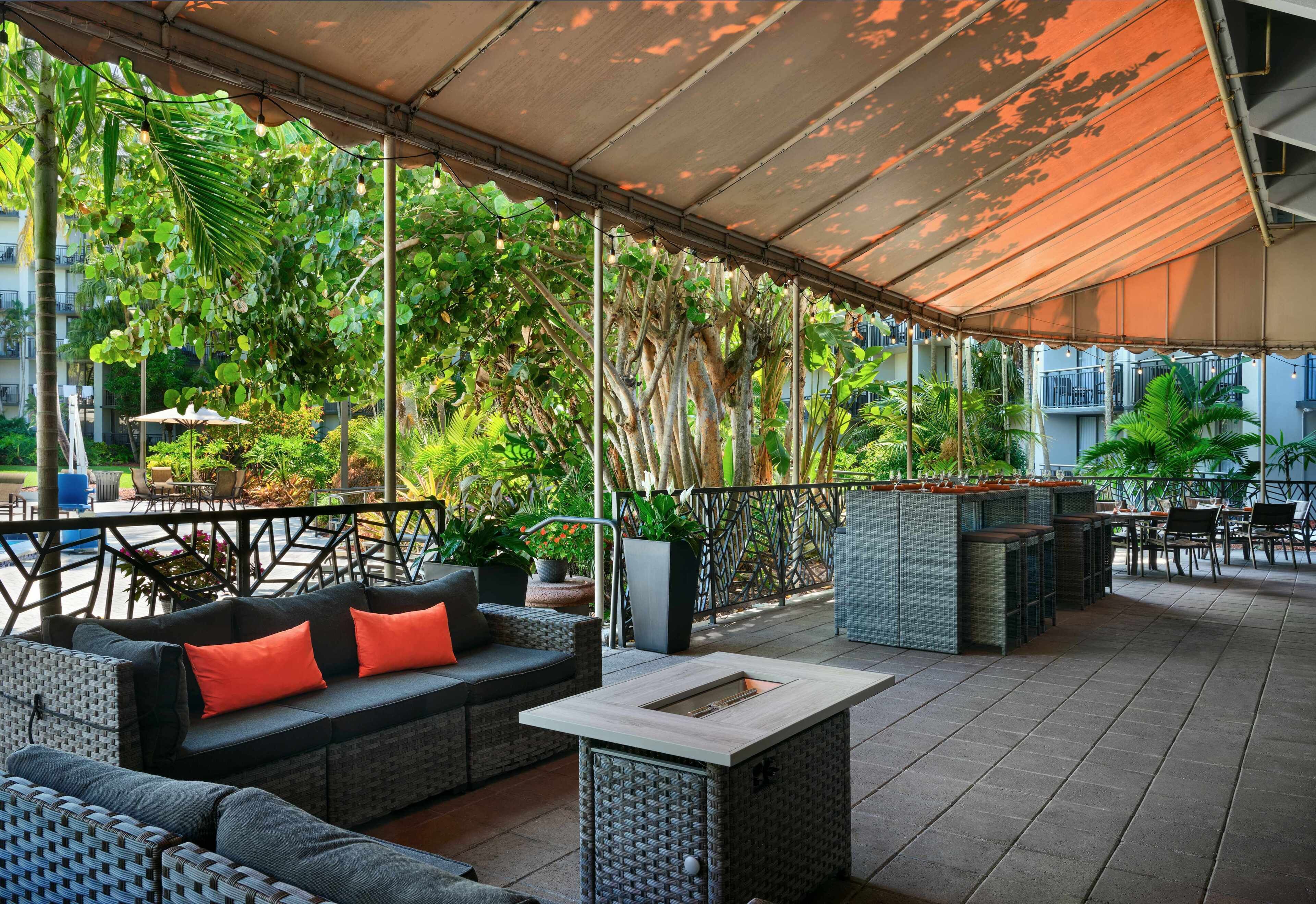 Un espacio al aire libre con mobiliario de mimbre, una mesa de centro y una pérgola que proporciona sombra.