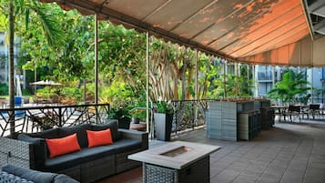 Un espacio al aire libre con mobiliario de mimbre, una mesa de centro y una pérgola que proporciona sombra.