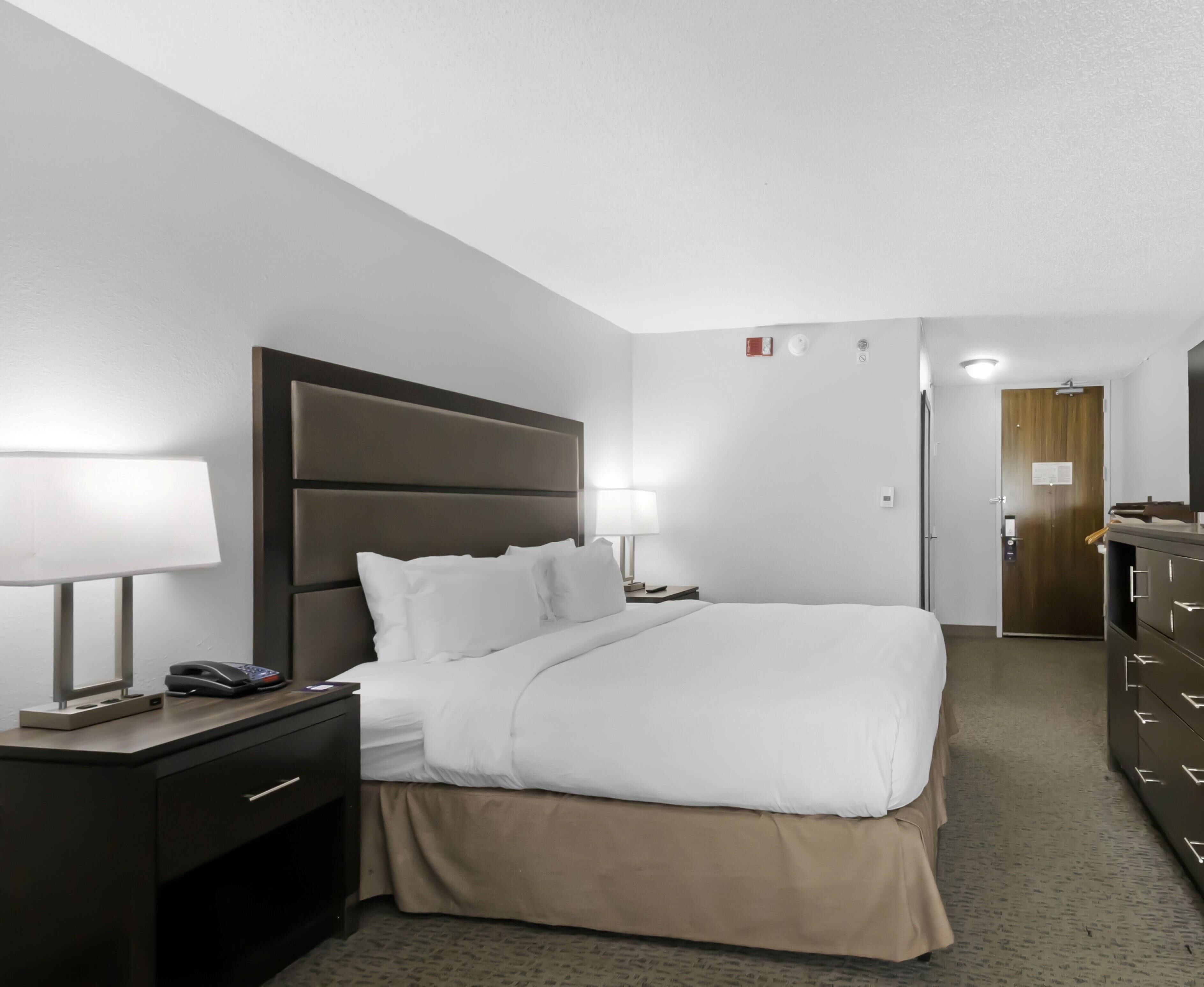 A hotel room with a bed, bedside lamps, a telephone, a dresser, and a door.
