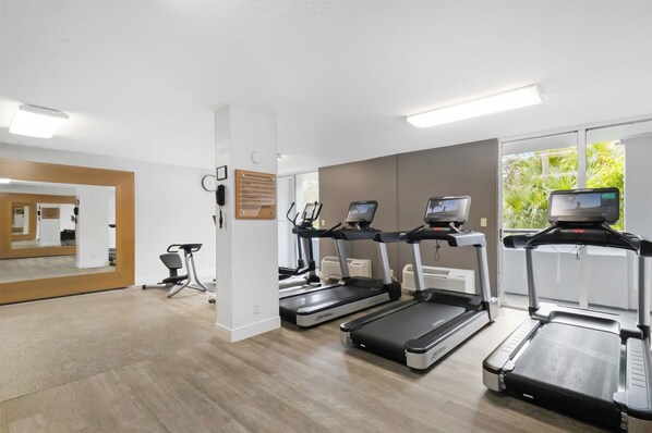 Un gimnasio equipado con cintas de correr, una bicicleta estática y un espejo.