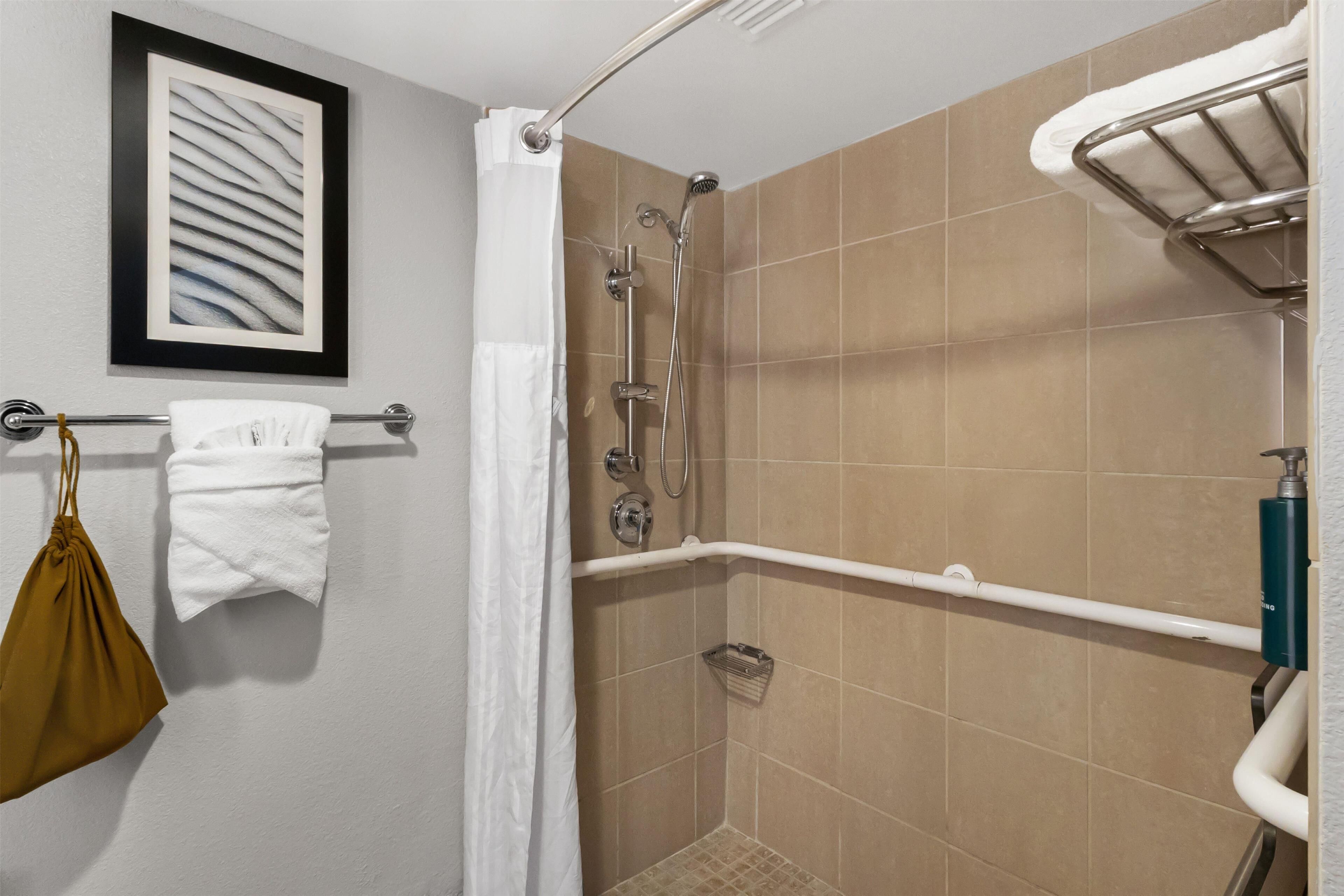 A shower area with a glass door, a towel rack with a white towel, a metal showerhead, and a framed abstract artwork on the wall.