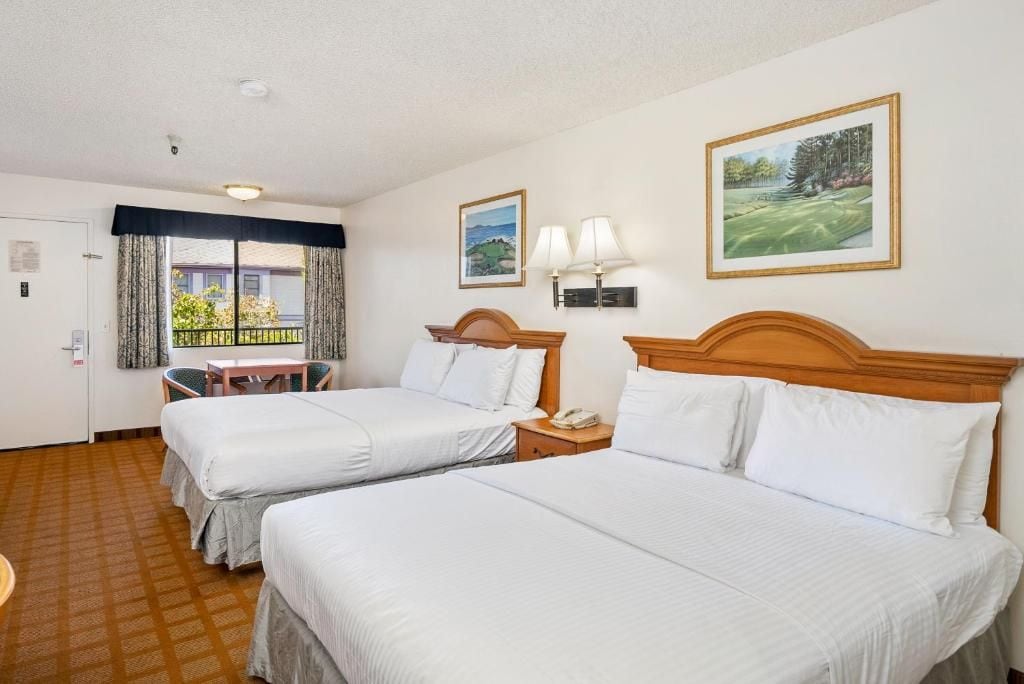 Une chambre d’hôtel avec deux lits, une petite table, une chaise et une fenêtre avec des rideaux.
