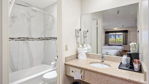 Un baño moderno con ducha de mármol, lavamanos con espejo y ventana con cortinas.