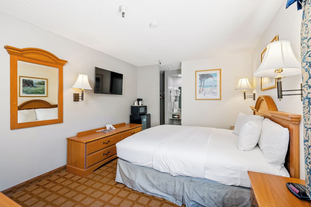 Une chambre d’hôtel équipée d’un lit, d’une commode en bois, d’un téléviseur à écran plat et de lampes fixées au mur.