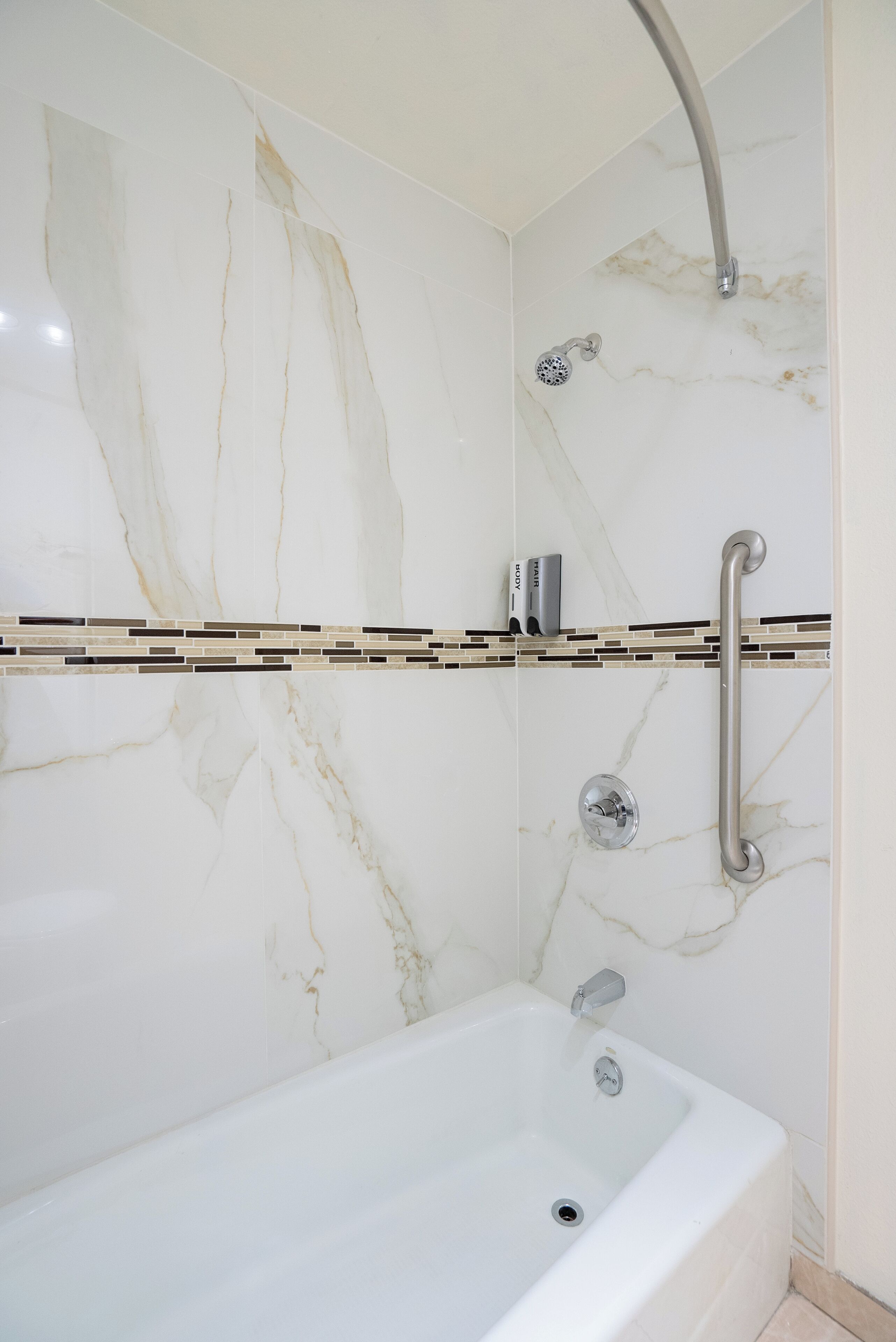 A modern bathroom with a marble wall, a shower with a handheld showerhead, and a bathtub.