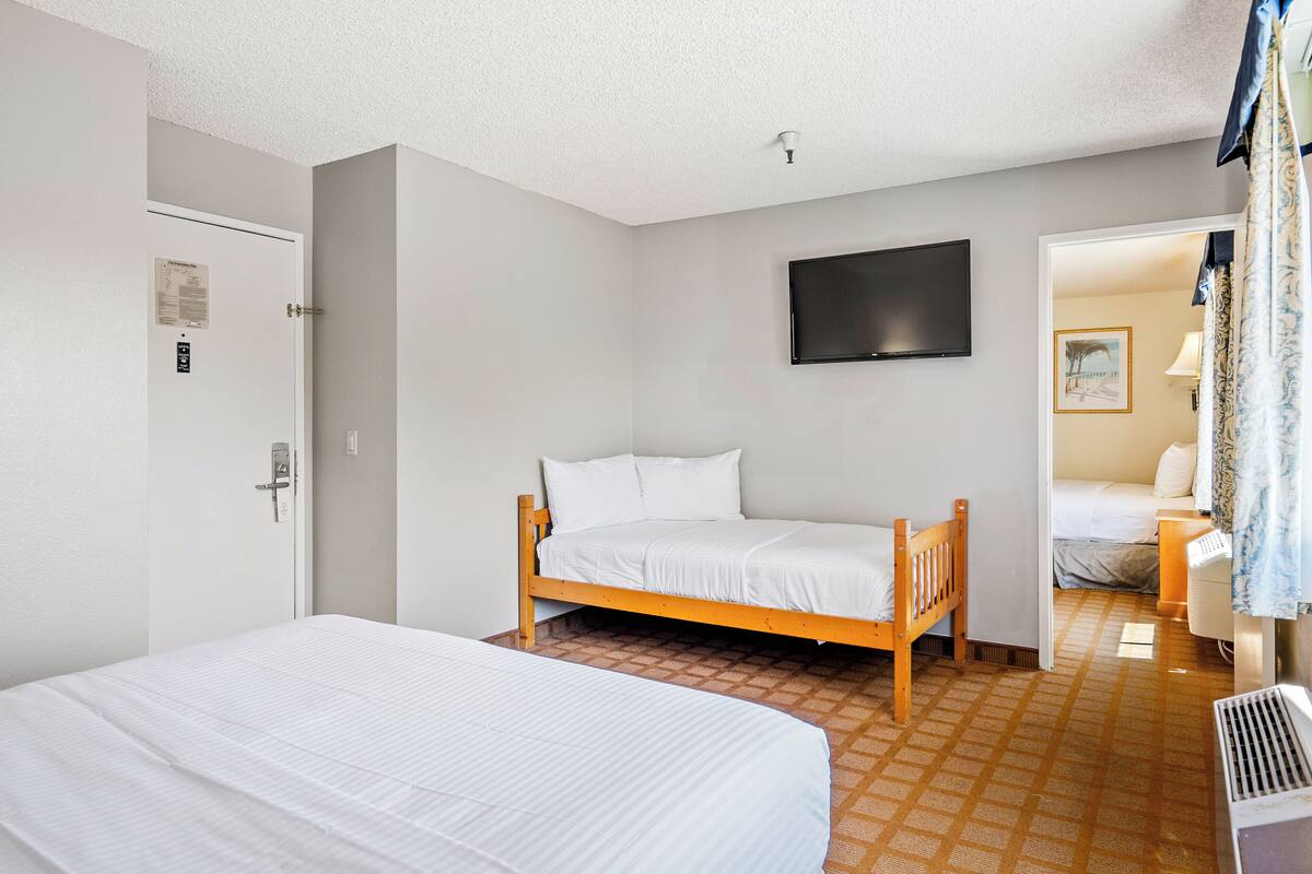 Une chambre d’hôtel avec un lit simple, un deuxième lit, un téléviseur fixé au mur et une porte dotée d’une serrure de sécurité.