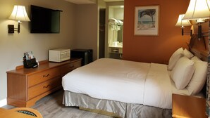 Habitación de hotel con cama, escritorio con lámpara, televisión, microondas y refrigerador pequeño.