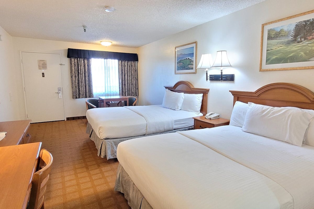Une chambre d’hôtel avec deux lits, un bureau, une chaise, une table et une fenêtre avec des rideaux.