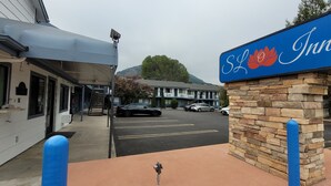 Señal de Sloth Inn con un pilar de piedra y bollards azules, un estacionamiento con autos y un edificio con toldo gris.