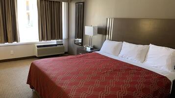 Habitación de hotel con una cama grande, una ventana con cortinas, una mesita de noche con lámpara y un espejo instalado en la pared.