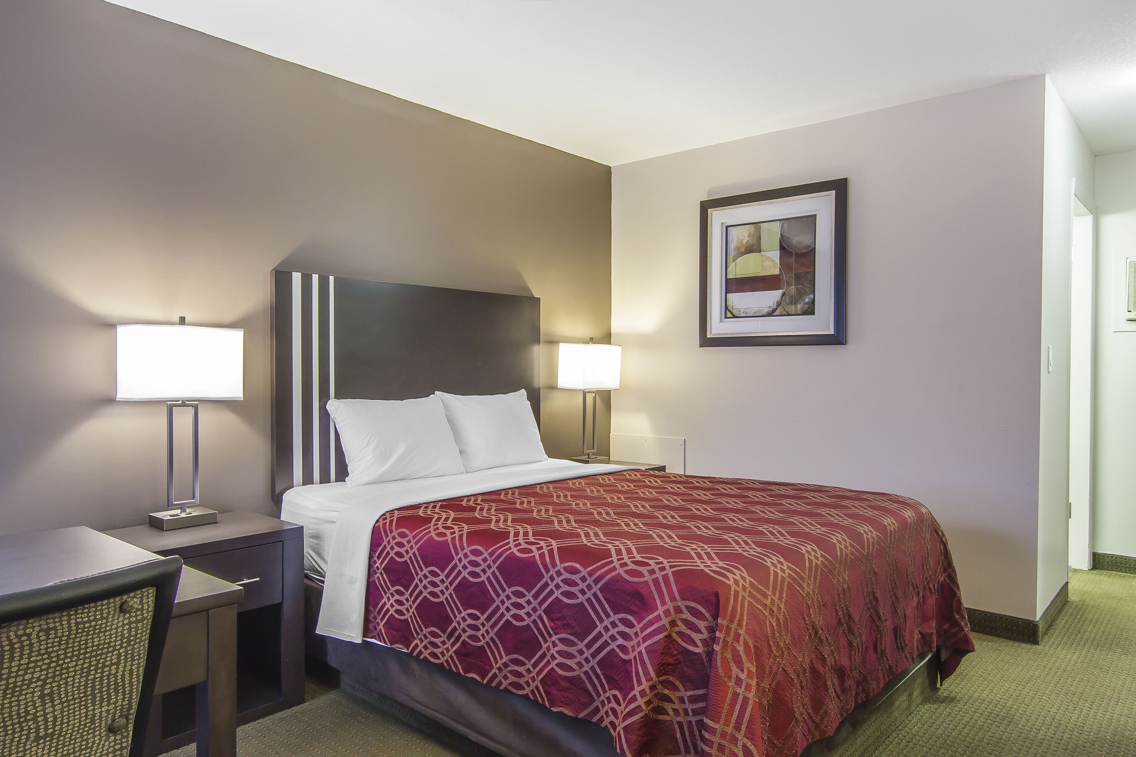 A hotel room with a bed, bedside lamps, a desk, and a chair.
