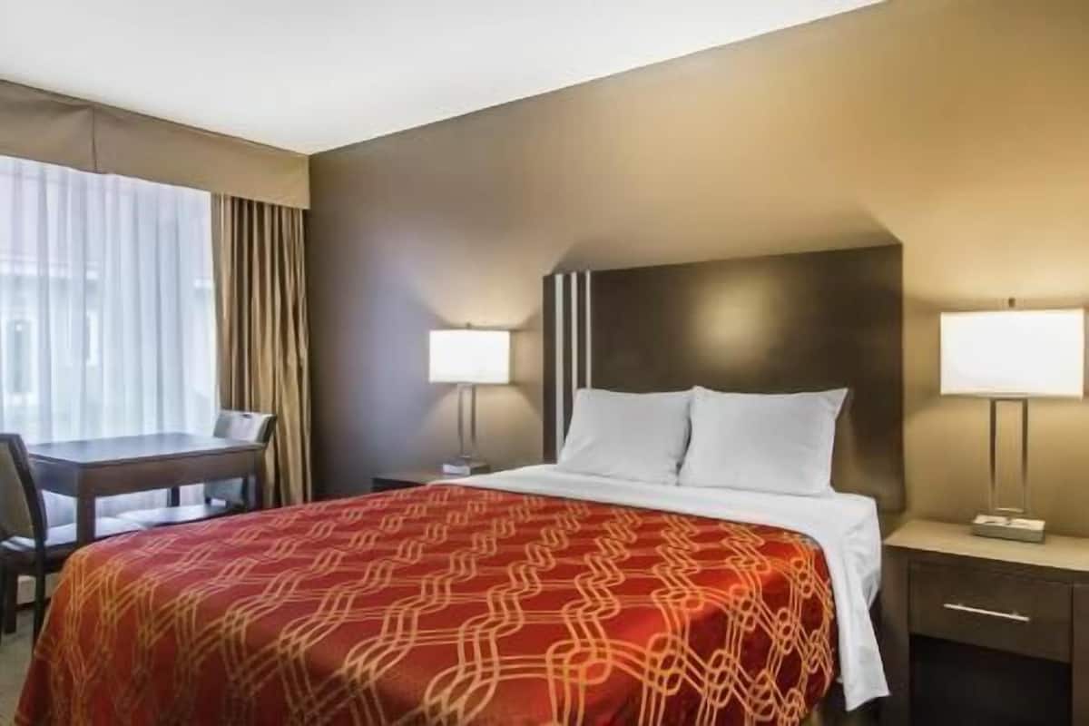 Hotellihuone, jossa on sänky, yöpöydät, lamput, työpöytä ja tuoli.