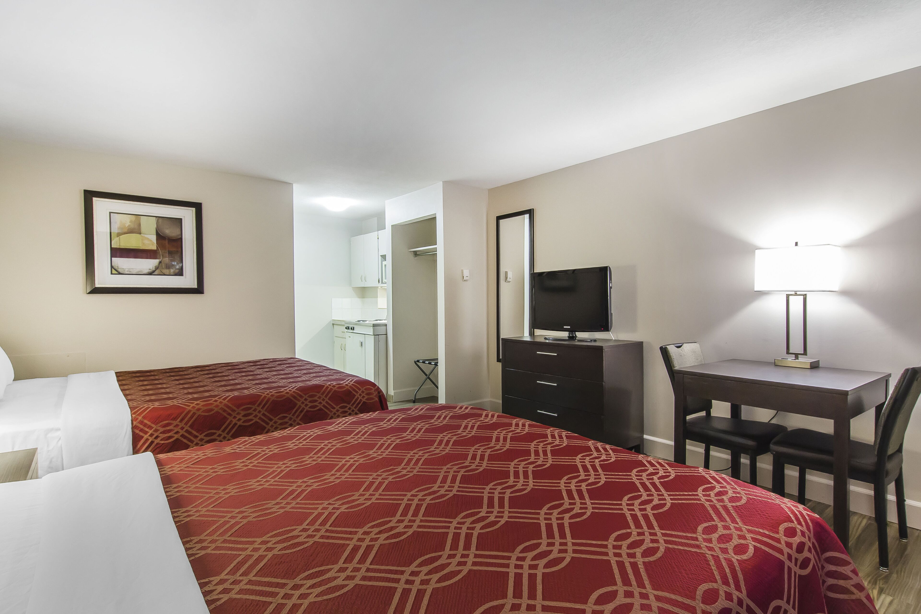 A hotel room with two beds, a desk with a chair, a TV, and a lamp.