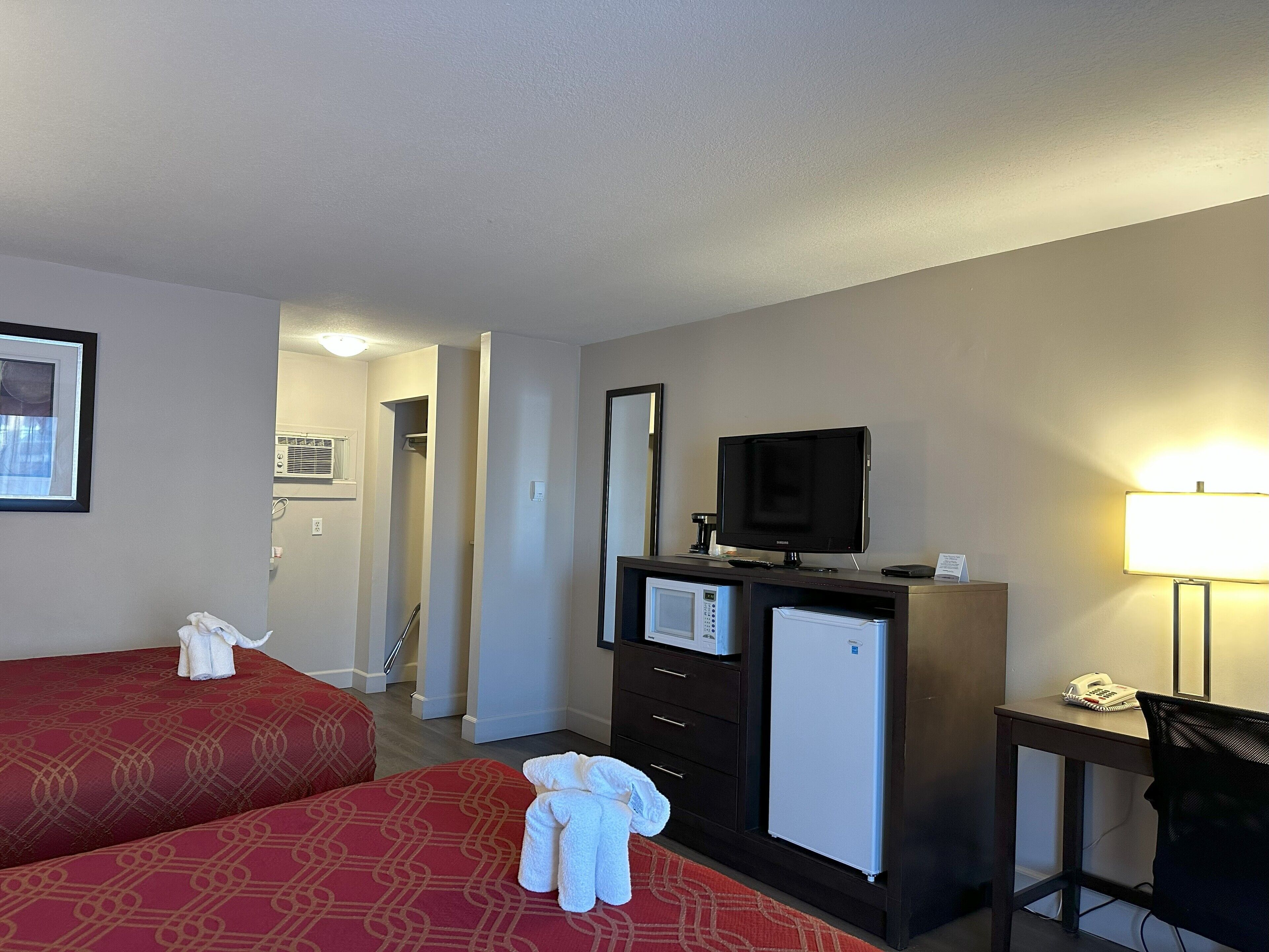 Habitación de hotel con dos camas, televisión, escritorio con lámpara, refrigerador y teléfono.