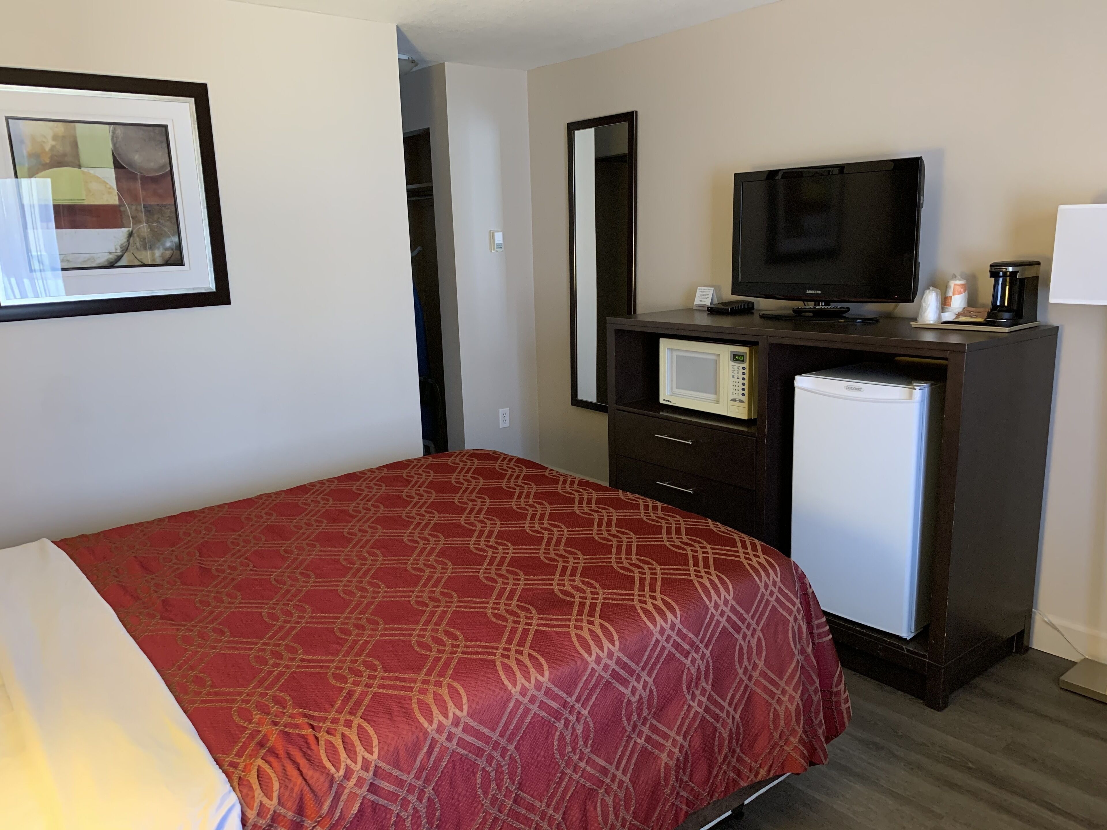 A hotel room with a bed, a television, a microwave, and a refrigerator.
