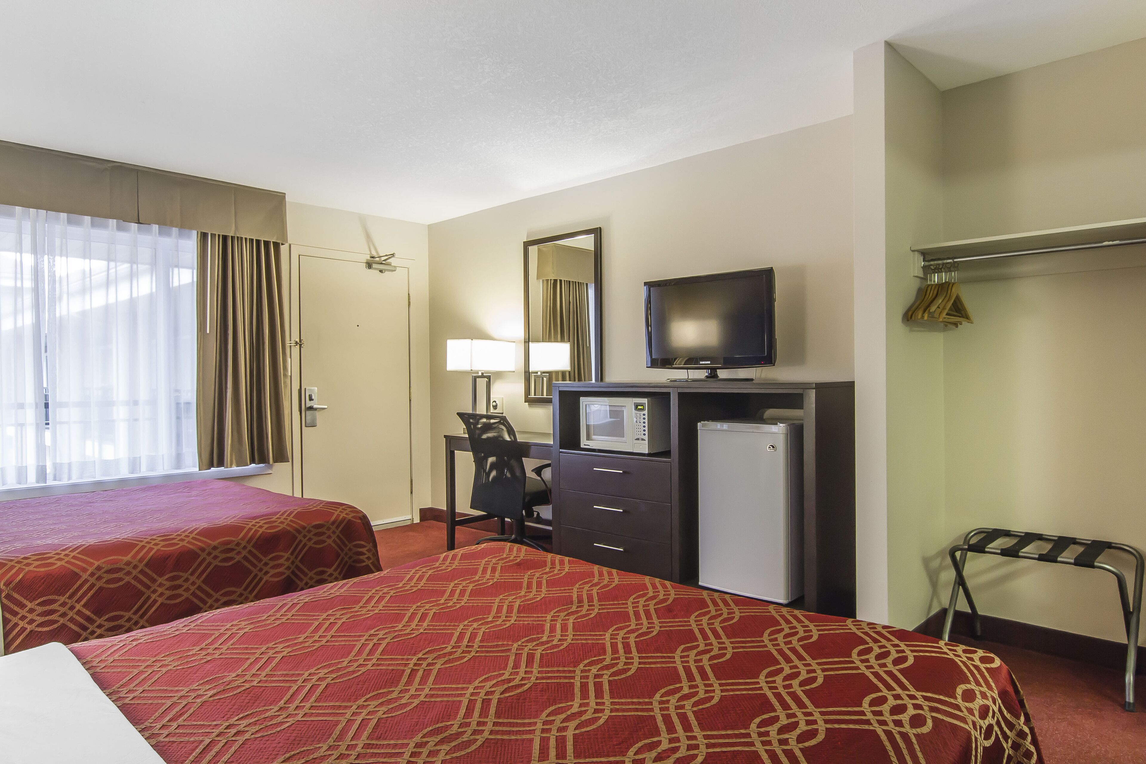 A hotel room with two beds, a desk with a computer, a television, a mirror, and a coat rack.