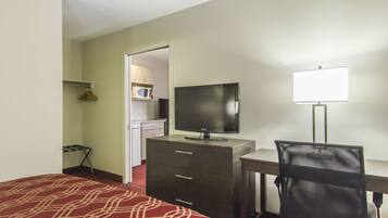 Habitación de hotel con cama, escritorio y silla, televisión, lámpara de escritorio y un microondas al fondo.