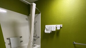 Un baño con bañera, ducha y pared verde.