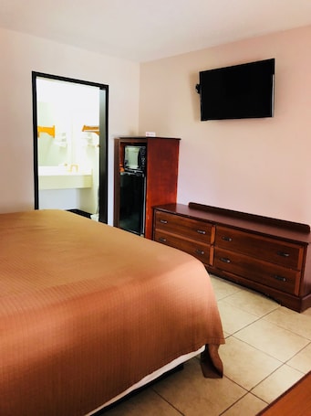 A hotel room with a large bed, a wooden dresser, a television mounted on the wall, and a microwave built into the dresser.