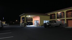 Un motel con zona de estacionamiento techada, un edificio de dos pisos con balcones y una bandera afuera.