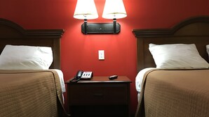 Habitación de hotel con dos camas, una mesita de noche con teléfono y control remoto, y lámparas fijadas a la pared.