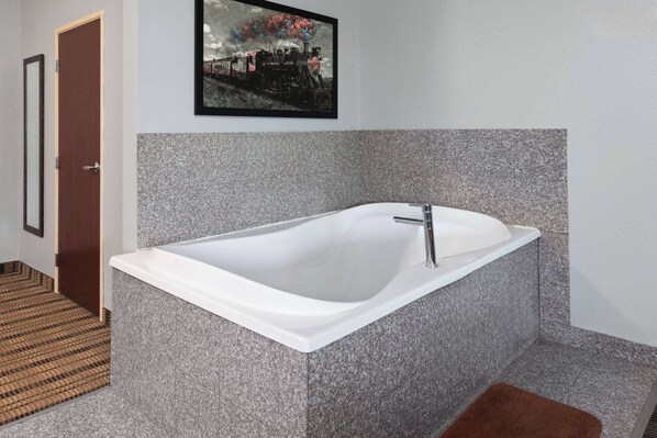 A modern bathroom with a freestanding bathtub, a framed picture on the wall, and a patterned floor. - AmericInn by Wyndham Grinnell (Grinnell)