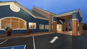A building with a blue exterior, large windows, and a parking lot with directional arrows. - AmericInn by Wyndham Grinnell (Grinnell)
