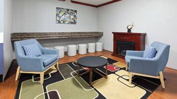 A living room with two blue armchairs, a round table, a patterned rug, a fireplace, and a wall art piece.
