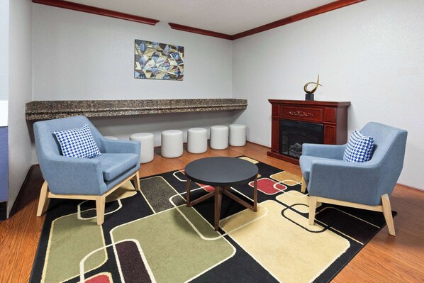 A living room with two blue armchairs, a round table, a patterned rug, a fireplace, and a wall art piece. - AmericInn by Wyndham Grinnell (Grinnell)